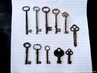 Photo showing 11 antique skeleton lock keys laid out on lined paper background.