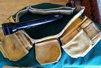Top view of yellow-tan leather tool pouch laid flat showing multiple pouches and a large black metal flashlight resting inside.