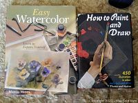 Front cover of two art instruction books: Easy Watercolor by Marcia Moses with floral watercolor painting and How to Paint and Draw by Thames and Hudson with an artist's hand painting with palette.