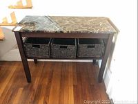 Front view of the sofa table showing the dark wood frame and marble-like top with three wicker baskets underneath on the lower shelf.