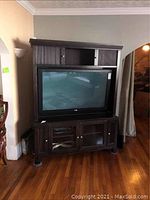 Front angled view of entire entertainment console with TV inserted (50" TV not included) showing upper and lower sections, cabinet doors, open shelves, and legs.