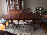 Full view of the solid cherry wood dining table with claw feet set in a dining room with matching chairs, showing the polished finish and wood grain pattern on the tabletop, with some visible wear on the feet.