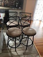 Four black steel swivel bar chairs with beige microfiber padded seats arranged in a kitchen/bar area.