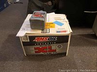Box containing 12 quarts of AMSOIL Synthetic Motor Oil XL SAE 5W-20, with one quart placed on top of the box.
