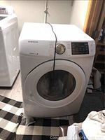 Front view of the white Samsung gas dryer showing the door, control panel, and power cord on top.