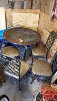 Photo showing round patio table with dark slate inlay and four matching metal frame chairs with tan vinyl seats, situated in a garage with plywood walls.