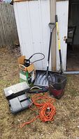 Full view of lot items including shovels, extension cord, masonry sprayer box, sprinkling device, garden basket, black plastic tray, all placed in front of white shed.
