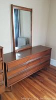 Photo of full dresser with mirror showing wooden construction, six drawers, recessed handles, and surface wear.