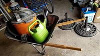 Wide shot showing wheelbarrow holding the Rigid shop vac and watering can, with other workshop items in background.
