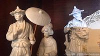 Two Fitz and Floyd Asian-inspired white ceramic figurines, male and female, holding umbrella, standing on wooden surface