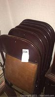 Six brown metal folding chairs stacked, showing the metal frame and vinyl seating in used condition.