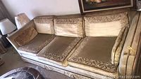 Vintage sofa with beige and gold fabric upholstery, three seat cushions, visible wear and staining.