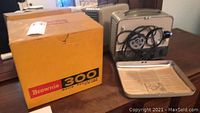 Kodak Brownie 300 movie projector, metal tray, and original yellow box on table.