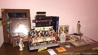 Overview of religious decor items showing framed paintings, books, statues, and resin Last Supper diorama, plus holy water bottle.