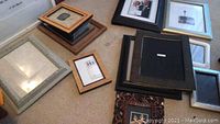 Various picture frames laid out on carpet, showing multiple frame sizes and finishes including a distressed white frame and dark wood frames.
