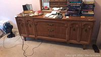 Full view of wooden dresser with various items on top including books, calculator, and decor.