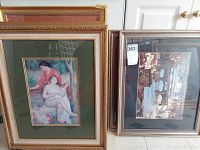 Eight framed artworks stacked against a white door, showing a mix of styles including a figurative painting of two women in an ornate frame and others with cityscape images.