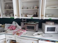 Photo of kitchen counter with Oster toaster oven, Hamilton Beach microwave, Osterizer blender, and cabinets with dishware inside.
