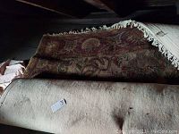 Photo of the rugs showing rolled up area rug and runner with fringe and traditional pattern colors.