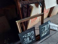 Two large decorative frames leaning against boxes on a floor, showing wear, scuffs and surface damage.