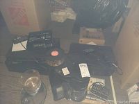 Lot overview showing audio/video devices and coffee maker on wooden floor near cardboard boxes
