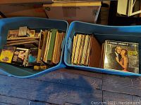 Two large blue bins filled with assorted vinyl records, cassette tapes, and CDs in cases and sleeves