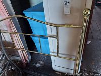 Photo of damaged end of metal bed frame showing loose knob and brass/golden finish