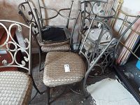Six metal frame dining chairs grouped closely together showing seated cushion tops and ornate backrests, some cushions show wear and one cushion cover partially removed.