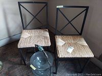 Two black metal frame rush chairs with woven seats showing wear and stains on a carpeted floor.