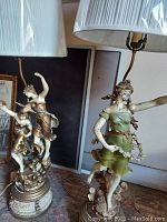 Pair of figure lamps showing overall height, pedestal bases, shades, and sculptural female figures.