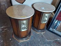 Pair of dark wood speaker end tables with round light marble tops, showing scratches and scuffs on base