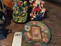 Photo showing the decorative plate with roses and cherubs, the flower and figures holder figurine, and the Santa Claus music box figurine on a wooden surface.