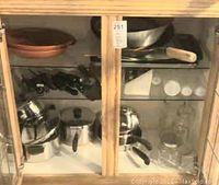 Wooden cabinet shelf containing cookware, glass carafes and first view of French press units