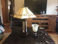 Two metal and glass table lamps together on a black surface in a living room, showing lamp sizes and overall appearance.