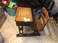Side view of antique child's school desk showing wooden seat and slanted wooden desktop with metal frame.