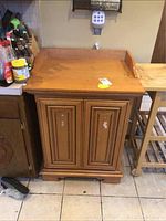 Front view of wooden kitchen cabinet with backsplash, two paneled doors, surface stains, and stickers.