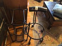 Side view of black metal rolling chair frame designed to hold a fitness ball seat and a metal rack for holding water bottles, showing caster wheels and curved armrest on chair frame.