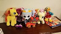 Multiple stuffed animals seen including yellow, blue, and pale yellow My Little Ponies, TY dog plush with hat, red Lego Movie cat character, and vintage Ludwig Duck with original box.