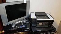 Lexmark printer and Sylvania TV seen together on a black surface with cables visible