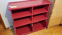 Front view of red enamel bookcase showing shelving and tilt-out compartments.