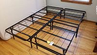 Photo of the two-piece metal bed frame clipped together in a room with hardwood floor and window in background, showing the full structure and grid design.