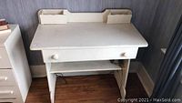 Front view of white painted wood desk showing drawer, back and side edges, and lower shelf.