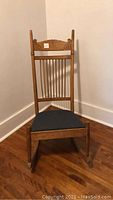 Front view of antique oak rocking chair showing carved back detail and upholstered seat.