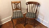 Two antique wooden chairs with matching plaid upholstered seats positioned side by side on a hardwood floor near a white wall.