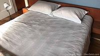 Bedsheet with two pillows covered by a light-colored duvet cover spread on bed.