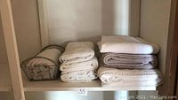 Multiple towels folded and stacked in two piles alongside a metal wire basket on a shelf.