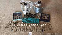 Full view of the lot showing the collector spoons laid out, boxed Seagull Pewter knife sets, silver plated creamer and sugar bowl, pewter cups, ice bucket and teapot.
