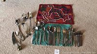 Photo showing full lot of cutlery and silverware laid out on the floor with colorful cloth mats, displaying forks, spoons, knives and serving pieces.