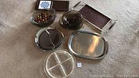 All items displayed on carpet, including metal and glass serving trays and platters with clear and polished finishes.