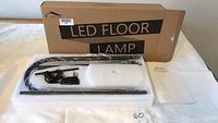 Photo showing LED floor lamp parts in original foam packaging with cardboard box in back labeled 'LED FLOOR LAMP'.